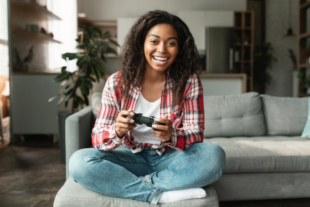 Person sitting cross-legged on a couch, smiling and holding a video game controller in a modern living room setting.